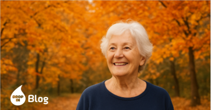 Ältere Frau, die in einem herbstlich verfärbten Wald lacht, umgeben von bunten Blättern und warmem Sonnenlicht.“